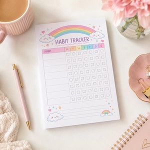 May include: A rectangular habit tracker notepad featuring a colourful rainbow and smiling clouds at the top. The page includes a grid with columns for days of the week labelled M, T, W, T, F, S, S and rows for habits. The text HABIT TRACKER is printed in purple.