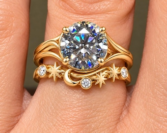 May include: A gold ring set consisting of two bands. The top band features a large, round, faceted clear stone held by four prongs. The bottom band is adorned with small clear stones, star-shaped accents, and a crescent moon shape.