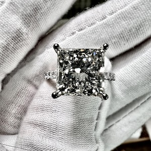 May include: A square-shaped diamond engagement ring with a white gold band and a row of smaller diamonds on each side of the center stone.