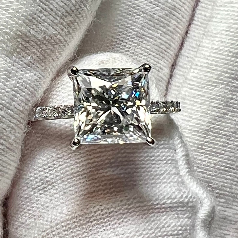 May include: A silver engagement ring with a large, square-cut diamond center stone and a band of smaller diamonds.