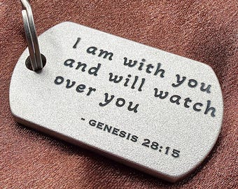 May include: A rectangular silver-toned metal tag with rounded corners and a metal split ring attached. The surface features the engraved black text: I am with you and will watch over you - GENESIS 28:15. The tag has a matte, textured finish.