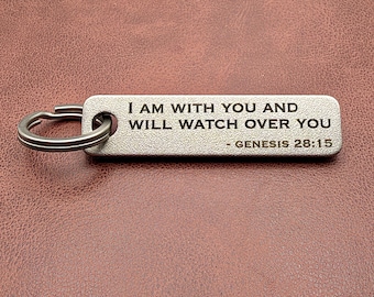 May include: A rectangular silver-toned metal keychain with a textured surface. The text "I AM WITH YOU AND WILL WATCH OVER YOU - GENESIS 28:15" is engraved in black on the front. A circular metal split ring is attached to the left side.