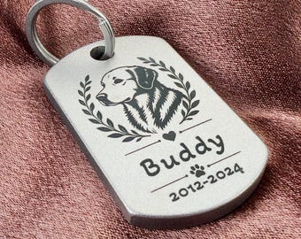 May include: A silver-toned metal pet tag with a rounded rectangular shape and a split ring. The tag features an engraved illustration of a dog head framed by laurel leaves, a small heart, the name Buddy, a paw print, and the years 2012-2024.