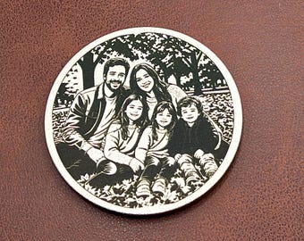 May include: A circular metal disc featuring a high-contrast black and white laser-engraved image of a family of four. The engraving depicts two adults and two children sitting together outdoors in a park setting with trees visible in the background.