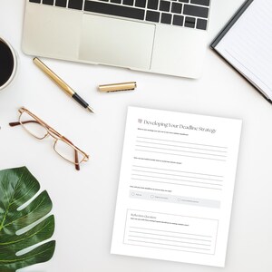 Peut inclure: Sc&egrave;ne de bureau avec un ordinateur portable, un stylo dor&eacute; et une feuille de papier intitul&eacute;e "Developing Your Deadline Strategy". On y trouve &eacute;galement une paire de lunettes, une tasse de caf&eacute; et un bloc-notes.
