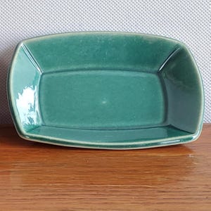 Może przedstawiać: Prostokątne ceramiczne naczynie z zaokrąglonymi rogami, pokryte błyszczącą, głęboką szmaragdowo-zieloną glazurą. Naczynie ma lekko nachylone ścianki oraz gładką, odbijającą światło powierzchnię o jednolitym kolorze na całej swojej powierzchni.
