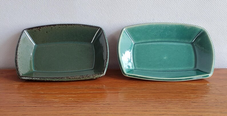 Może przedstawiać: Dwie prostokątne ceramiczne miseczki z lekko zakrzywionymi bokami i zaokrąglonymi rogami. Miseczka po lewej stronie ma ciemnozieloną glazurę z teksturowanym, nakrapianym brzegiem, podczas gdy ta po prawej ma gładkie, błyszczące turkusowe wykończenie.