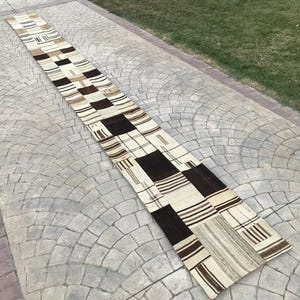 May include: A long, rectangular patchwork rug with a white background and brown stripes. The rug is made of different pieces of fabric sewn together.