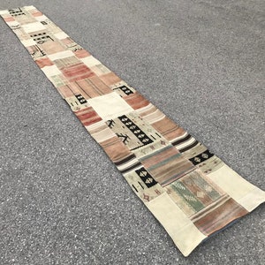 May include: A long, rectangular rug with a patchwork design. The rug is made of different fabrics and colours, including beige, brown, and red. The rug has a fringe on the edges.