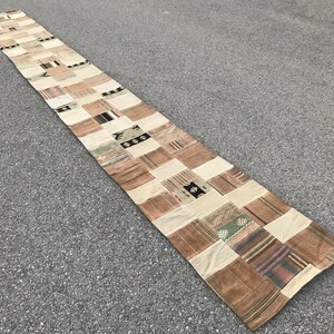 May include: A long, rectangular patchwork rug with a variety of colours and patterns. The rug is made of different fabrics and textures, and it has a rustic, vintage look.