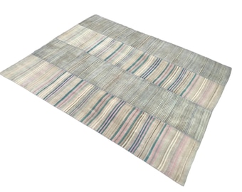 May include: A rectangular rug with a patchwork design. The rug features alternating sections of solid and striped patterns in shades of gray, with accents of pink, blue, and green. The rug is made of a soft, woven material.