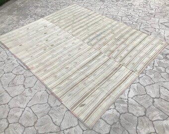 May include: A white and beige striped rug with a subtle floral pattern. The rug is folded in half and laid out on a stone surface.