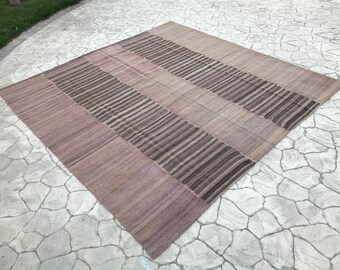 May include: A rectangular rug with a striped pattern in shades of brown and beige. The rug is made of a woven material and has a soft, textured surface.