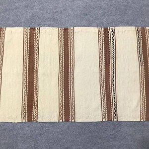 May include: A white woven rug with brown and black stripes. The rug has a fringe on all sides.