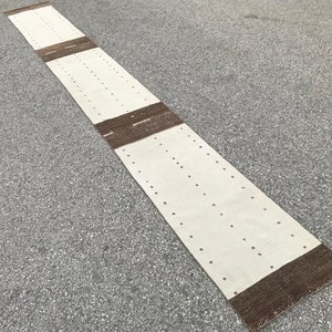以下が含まれることがあります： 縁に茶色のストライプが入った、長方形の白い敷物。敷物全体に、小さな穴が均等に開いています。