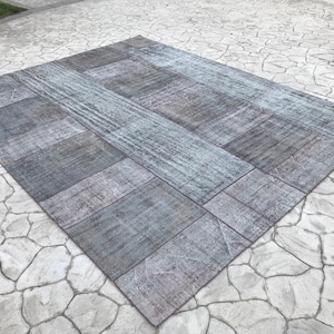 Pode incluir: Um tapete de patchwork com uma combinação de cores azul e cinza. O tapete é feito de diferentes pedaços de tecido costurados juntos. O tapete está colocado sobre uma superfície de concreto.