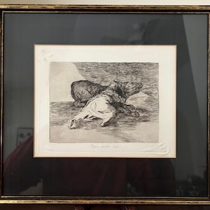 May include: Framed black and white etching depicting two figures in a distressed scene. The artwork is set within a gold-toned frame with a black mat. The etching is signed and numbered.