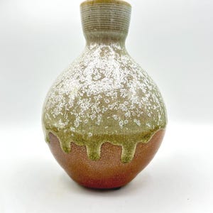 May include: A ceramic vase with a rounded body and a narrow neck. The lower portion features a textured reddish-brown clay finish, while the upper section is coated in a green glaze with a white crystalline drip pattern that cascades downward.