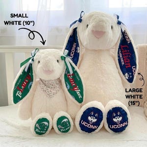 May include: Two white plush bunny rabbits. The smaller bunny is 10 inches tall and has green and white patterned ears with the text "Tulane". The larger bunny is 15 inches tall and has blue and white patterned ears with the text "UCONN".