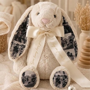 May include: A soft, cream-coloured bunny toy with long ears and a pink nose. The inside of the ears and the bottom of the feet display black and white photos. A cream ribbon is tied around the neck with the text "Some bunny loves you" and "Hug me forever".