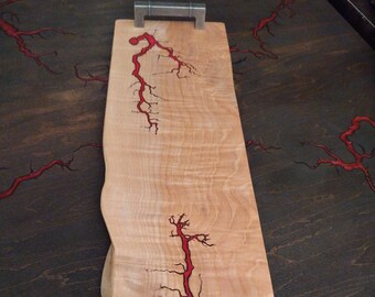 Curly maple charcuterie board with fractural burnings and Red epoxy inlay, sealed with food safe oil by "odies oil". Measures 22 1/2" x 7".