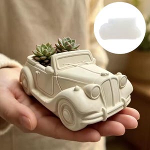 May include: A cream-coloured vintage car-shaped planter made of a solid material, featuring a hollow interior currently holding two small green succulent plants. The car design includes detailed headlights, a windscreen, and wheels.