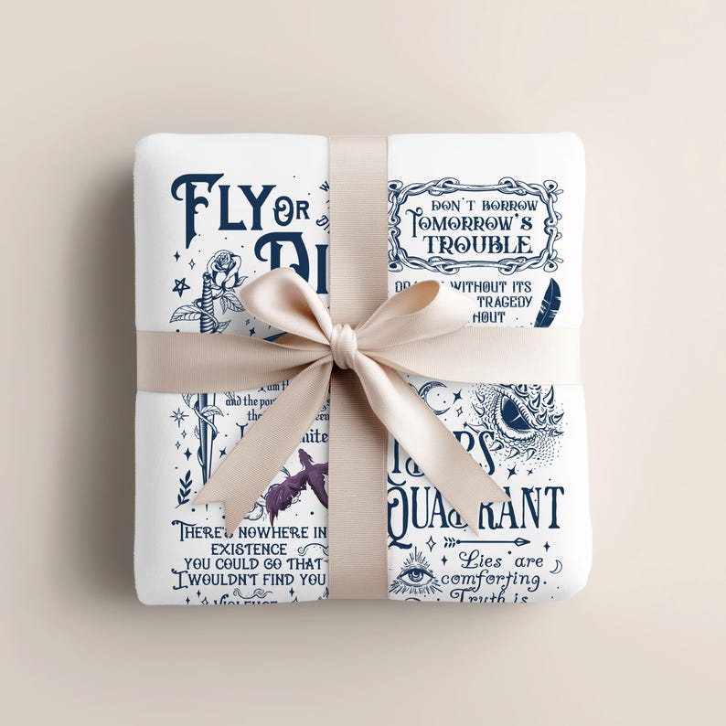 Op de afbeelding: Een witte deken met donkerblauwe tekst en illustraties, vastgebonden met een cr&egrave;mekleurig lint. De deken toont citaten en illustraties, waaronder een roos, een oog en een vleermuis. De tekst bevat zinnen als "Fly or Die" en "Don't Borrow Tomorrow's Trouble."