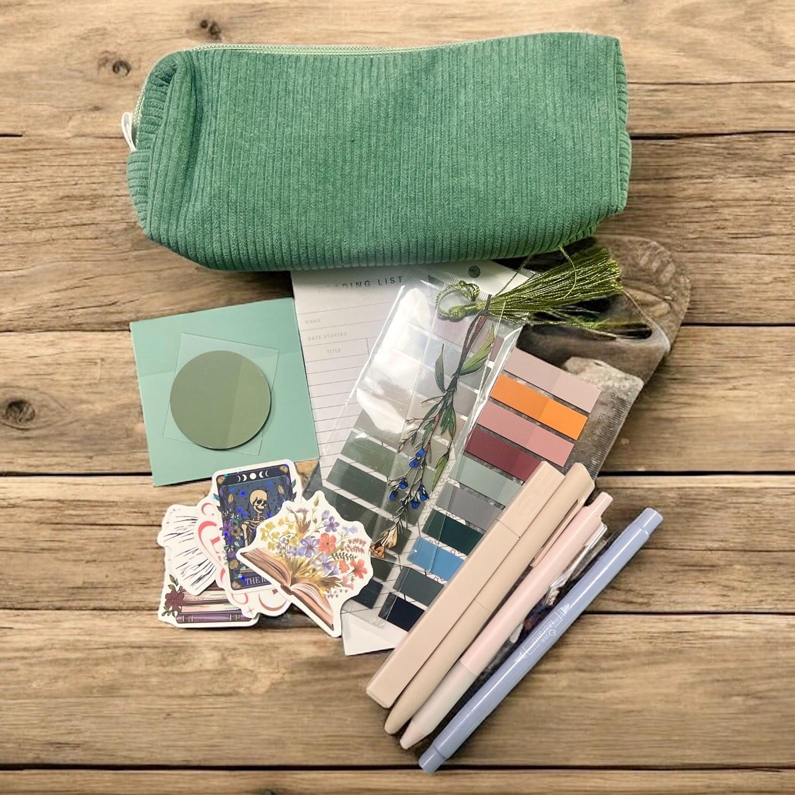 A green pencil case on a wooden surface surrounded by colorful pens, floral stickers, and a to-do list, conveying a creative, organized vibe.