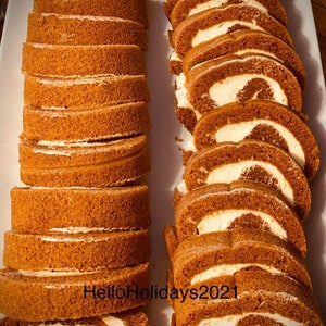 May include: A platter of sliced pumpkin roll cake with a creamy white filling. The cake slices are a warm brown color, and the filling is visible in the center of each slice. The cake is arranged on a white rectangular platter.