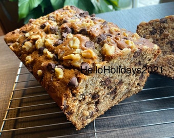 Può includere: Un pane alle banane con gocce di cioccolato e noci su una griglia metallica. Il pane è tagliato e mostra l'interno del pane.