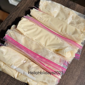 May include: Several clear plastic freezer bags filled with a light yellow batter, stacked on top of each other. The bags are sealed with pink zippers. The text "HelloHolidays2021" is written on a white label on one of the bags.