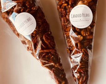 May include: Two clear plastic cones filled with candied pecans. The cones have labels that say "Candied Pecans" with a heart and the ingredients listed.