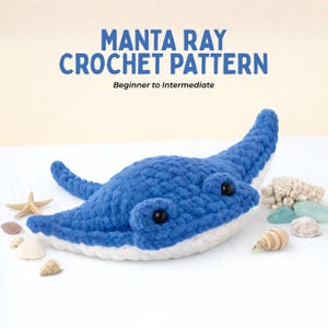 Op de afbeelding: Een blauwe gehaakte mantarog met zwarte ogen en een witte onderkant. De afbeelding bevat de tekst "Manta Ray Crochet Pattern" en "Beginner to Intermediate". Schelpen en een zeester liggen verspreid rond de mantarog.