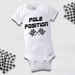 Puede incluir: Un body blanco para bebé con texto negro que dice "POLE POSITION" y dos banderas a cuadros negras y blancas cruzadas detrás del texto.