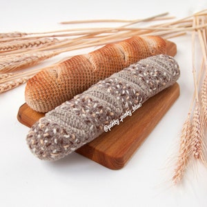 Op de afbeelding: Twee gebreide broodstaven op een houten snijplank. De broden zijn bruin en beige met een gespikkelde textuur. De plank is lichtbruin met een natuurlijke houtnerf.