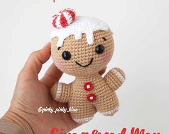 May include: Crochet pattern for a gingerbread man amigurumi toy. The gingerbread man is brown with white icing and red buttons. He is wearing a red and white candy cane hat.