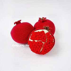 May include: Three crocheted pomegranates, one with the inside showing red seeds. The pomegranates are red and white.