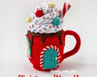 May include: Crochet Christmas mug house pattern. A red crocheted mug with a candy cane trim and a teal door. The mug has a white crocheted whipped cream topping with red and white sprinkles and a candy cane.