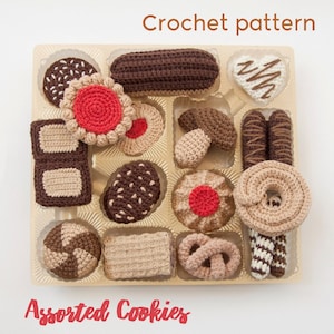 Könnte beinhalten: Eine Schachtel mit gehäkelten Keksen in verschiedenen Formen und Farben, darunter Schokolade, Vanille und Lebkuchen. Die Schachtel ist mit "Assorted Cookies" und "Crochet pattern" beschriftet.