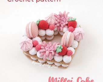 Op de afbeelding: Haakpatroon voor een hartvormige Milfei-taart. De taart is gemaakt van gehaakte lagen room, macarons, aardbeien en meringue. De taart is versierd met roze en groene details.