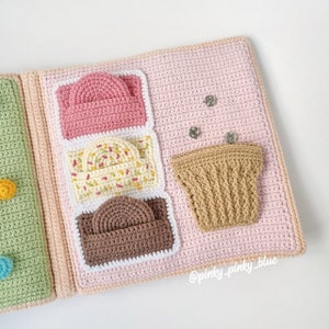 May include: A pink, white, and brown crocheted ice cream cone toy with a brown crocheted cupcake toy. The toys are attached to a pink crocheted fabric with white stitching.