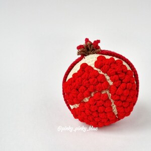May include: A crocheted pomegranate with red and white yarn. The pomegranate is round and has a brown stem on top.