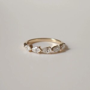 May include: A gold band ring featuring seven pear-shaped diamonds. The diamonds are set in a row, creating a delicate and elegant design. The ring is set against a white background, highlighting the sparkle of the gemstones.