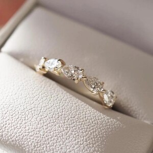 May include: A gold ring with multiple clear, oval-shaped gemstones set in a row. The ring is displayed inside a white, textured jewelry box.