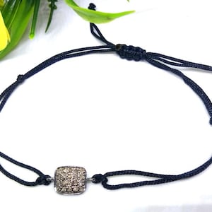 May include: A black adjustable cord bracelet with a square-shaped charm set with small white diamonds.
