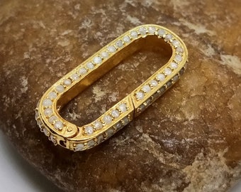 May include: A gold oval-shaped clasp with a row of small white diamonds around the edge.