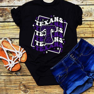 May include: Black t-shirt with a purple and white graphic design that says "Texans" with a leopard print letter "T".