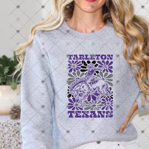 May include: A light gray crewneck sweatshirt featuring a graphic print of a cowboy riding a horse surrounded by purple and gray flowers. The text TARLETON TEXANS is printed in purple block letters above and below the central illustration.