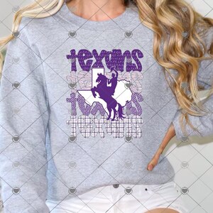 May include: A heather gray crewneck sweatshirt featuring a graphic print with the word texans repeated in various patterns. A purple silhouette of a person riding a bucking horse is centered over a white outline of the state of Texas.