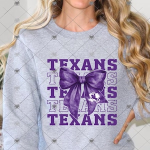 May include: A heather gray crewneck sweatshirt featuring the word TEXANS repeated in purple block lettering. A large, purple, watercolor-style bow is centered over the text, with a small white graphic of the state of Texas inside the bow.